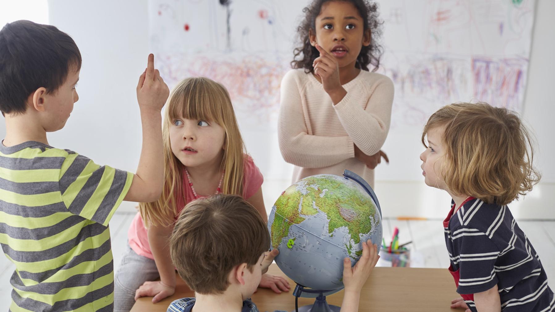A group of children talking to each other in a classroom around a globe